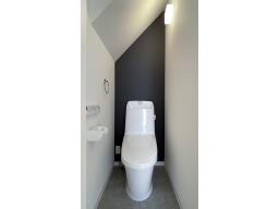 ブラックのアクセントクロスが効いたスタイリッシュなお手洗い。フチレス形状で汚れがたまりにくく、水アカや汚れが付きにくい、清掃性・快適性・デザイン性に優れた一体型シャワートイレ（LIXIL）です。（写真1階）